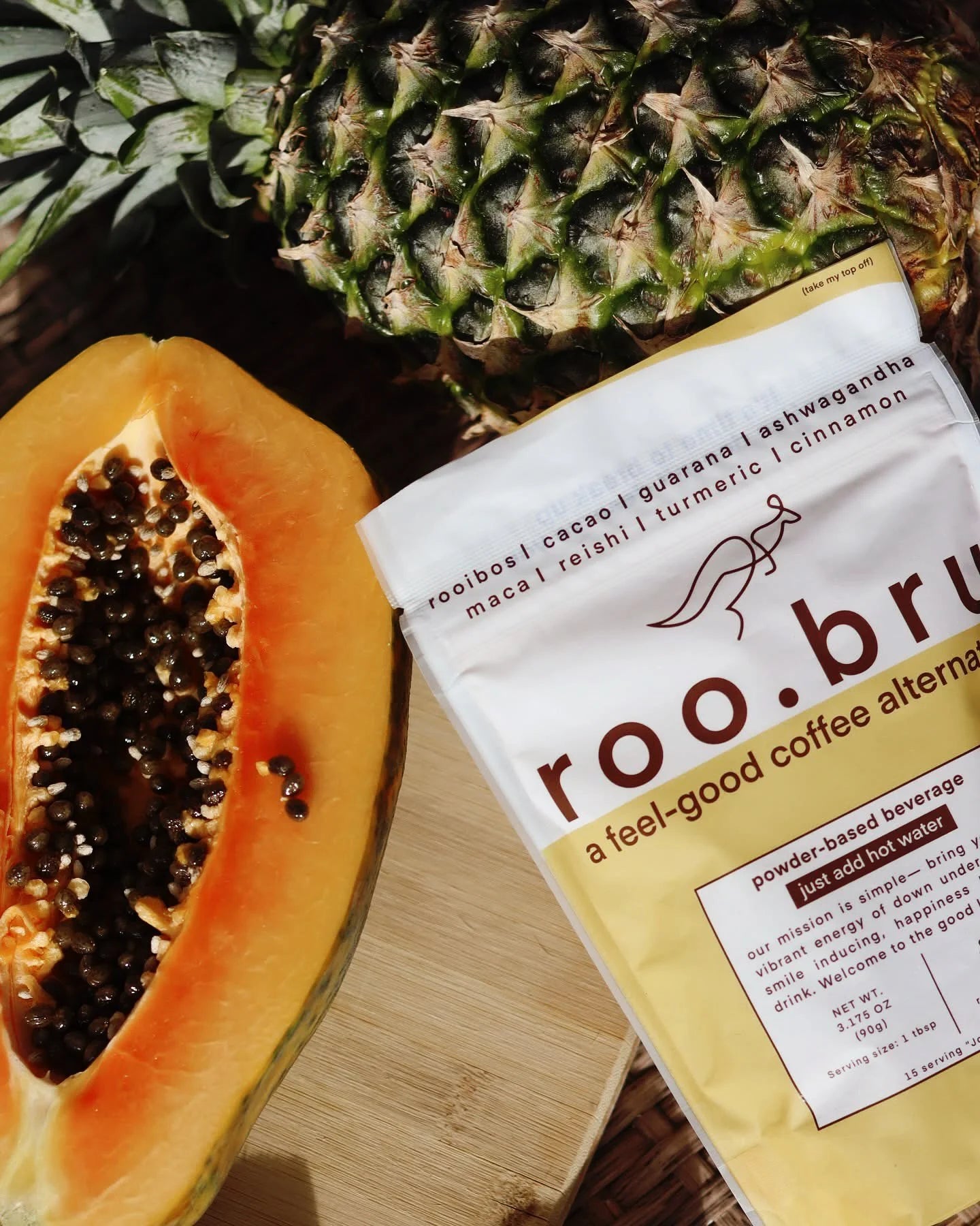 A roo.bru feel-good coffee alternative pouch beside fresh pineapple and sliced papaya