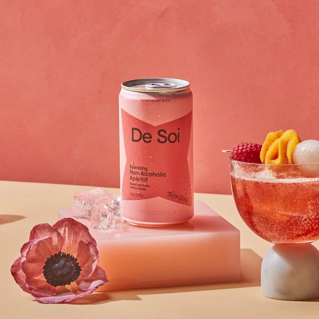 A pink De Soi sparkling non-alcoholic aperitif can styled with ice, an anemone flower, and a coupe